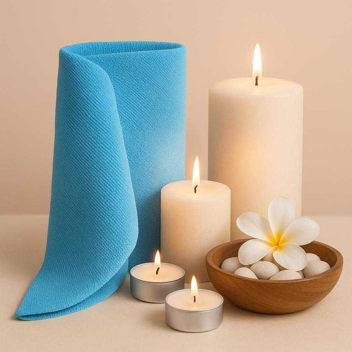 Vaskeklud i Mikrofiber - Skånsom Rengøring og Pleje i Blå, Beige, Grøn, Orange, Silver. The blue microfiber cloth is elegantly folded beside a set of aromatic candles in a serene spa setting, highlighting its gentle care properties.