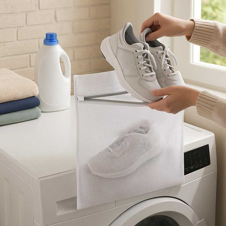 Vaskepose i høj kvalitet - Ideel til sko og større tekstiler, Beskytter tøj under vask, Tilgængelig i Medium og Large: A realistic laundry room setting where the bag is properly grounded on a washing machine, being actively used by hands placing a pair of shoes inside.