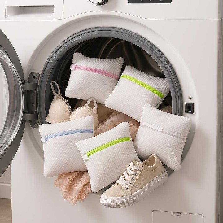 Vaskeposer i Mesh med Lynlås – Professionel Beskyttelse til Sko, Tøj og Undertøj i Flere Farver. Laundry room setting with multiple mesh laundry bags protecting delicate garments as they tumble in a front-loading washing machine, with items like shoes and lingerie peeking out from some bags.