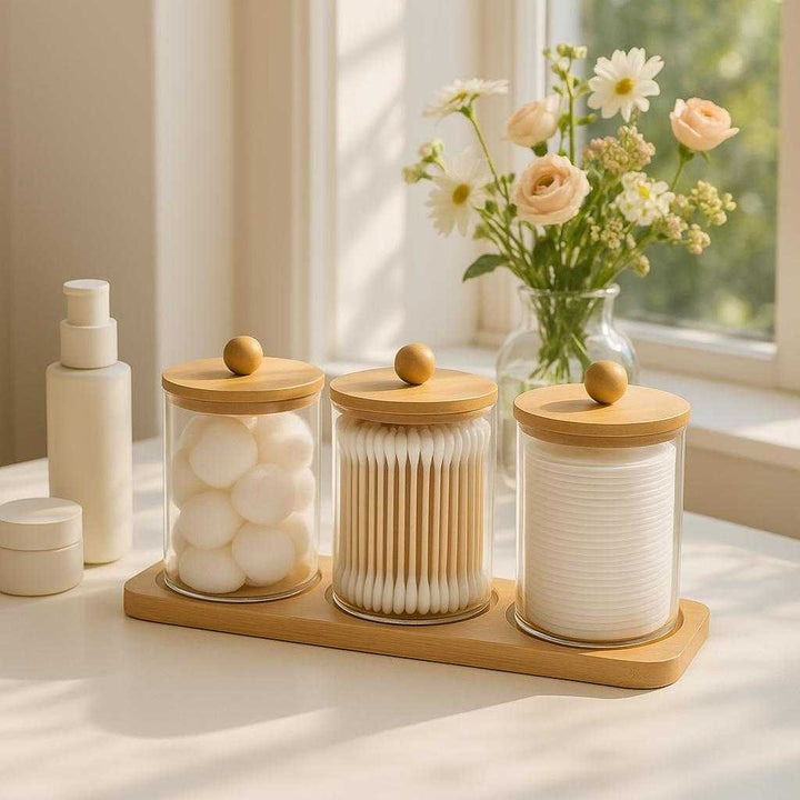 Vatpindeholdere i Glas med Bambuslåg og Bakke – Høj Kvalitet 3-delt Sæt. A bright, sunlit vanity table holds the glass cotton holder set filled with cotton balls and swabs, accompanied by minimalist skincare products and a vase of fresh flowers, creating an organized and inviting beauty corner.