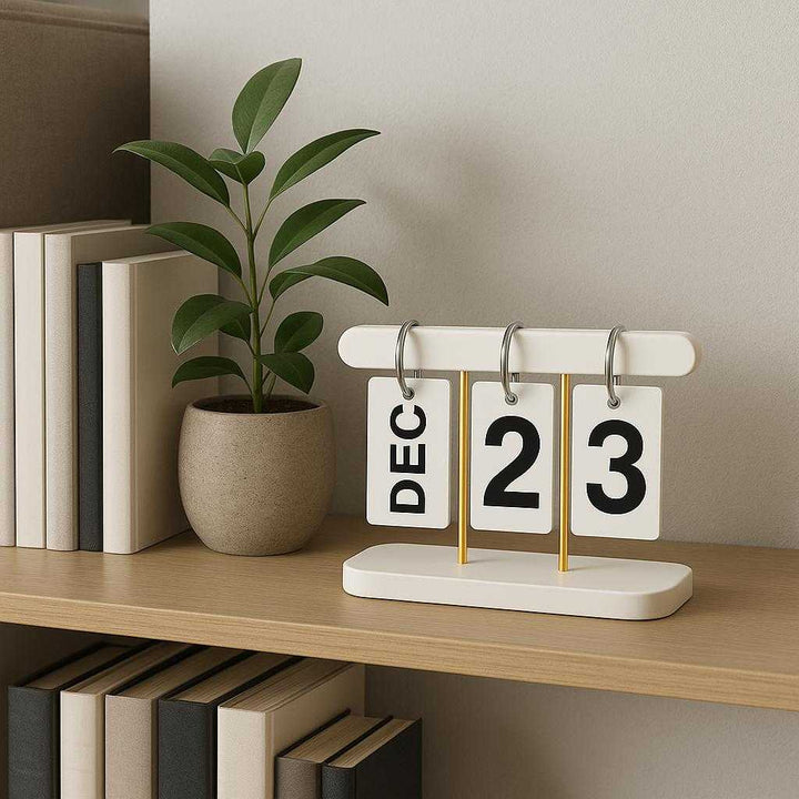 Vendekalender i Hvid og Sort med Minimalistisk Design – Professionel og Tidløs Kalenderløsning i Metal og Plastik. The chic calendar is prominently displayed on a modern living room shelf next to books and a potted plant, creating a professional and timeless ambiance.