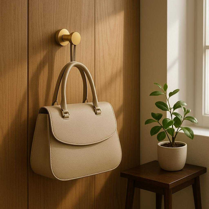 Vægknage i moderne design - Tilgængelig i guld, sort og lyseblå: A realistic entryway of a modern home where the gold wall hook is properly grounded on a wooden wall panel, actively used to hold a stylish handbag.