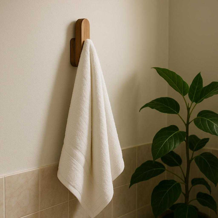 Vægknage i træ – Moderne og pladsbesparende løsning til opbevaring i entréen, badeværelset eller soveværelset. In a serene bathroom setting, the wooden hook is used to elegantly hang a luxurious white towel beside a lush green plant, creating a spa-like atmosphere with ambient lighting.