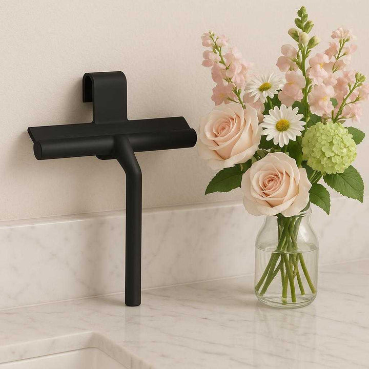 Vindueskraber i silikone - Effektiv og skånsom rengøring af vinduer, spejle og fliser. The elegant black silicone window scraper is displayed on a marble bathroom counter next to a vase of fresh flowers, emphasizing its stylish design and practicality.